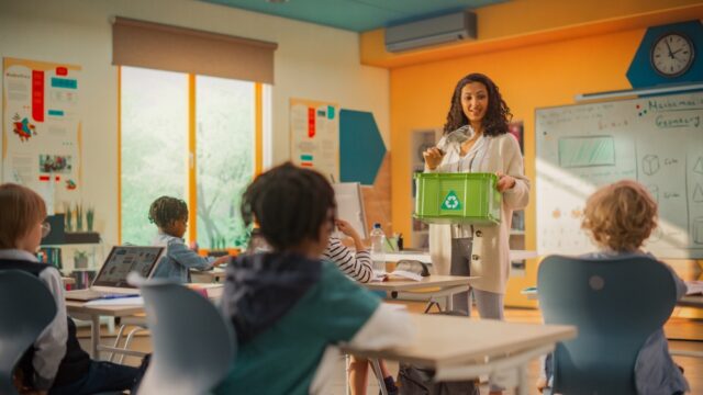 Elementary,School,Classroom:,Enthusiastic,Female,Teacher,Holding,An,Empty,Plastic